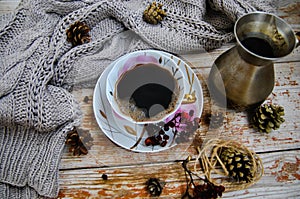 Porcelain cup of black coffee and coffeepot on the rustic background with winter decoration.