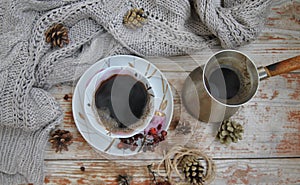 Porcelain cup of black coffee and coffeepot on the rustic background with winter decoration.