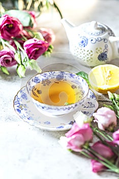 Porcelain cup of herbal green tea, lemon, mint and flowers on light grey background.