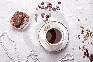 Porcelain cup of mocca coffee with natural chocolate, cocao beans, green coffe beans and neck beads around white provence