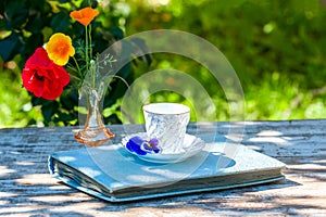 Porcelain cup of tea and beautiful spring flowers in vase on a wooden table in the garden. Summer party.