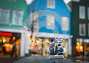 Porcelain figures of a boy and a girl kissing against a blurred background of blue houses in a festive evening light.Netherlands,
