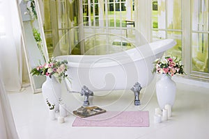 Porcelain freestanding bath in designed white bathroom. White luxurious bath, a bouquet of flowers in a large vase. Still life or