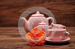A porcelain spotted tea cup and kettle and an orange rose