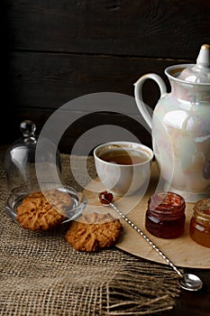 Porcelain tea kettle and teacup with green tea. Pressed roses on a wooden table. Three small jars of homemade berry jam on the woo