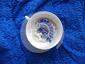 Porcelain teacup with jewelry on lacy background