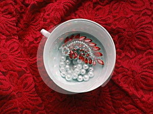 Porcelain teacup with jewelry on red lacy background