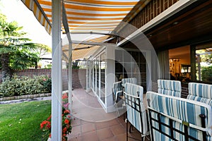 Porch of a detached house with glass latticework, striped awnings and a garden with a lawn and flowers photo