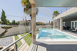 Porch of a single-family home with a swimming pool and palm trees, a metal railing overlooking the garden and shady wicker