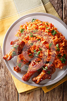 Porcion of African Jollof rice with fried chicken wings close-up on a plate. Vertical top view