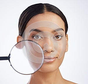 Poreless and flawless. Studio shot of an attractive young woman looking through a magnifying glass against a grey