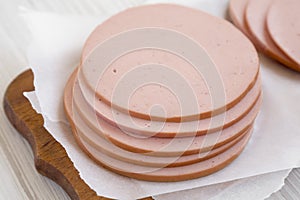 Pork bolgna meat slices on a rustic wooden board on a white wooden table, side view. Closeup photo