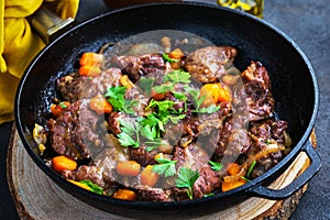 Pork cheeks stewed with vegetables in an iron pan, sliced bread, olive oil, with a dark background in a single shot above photo