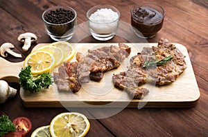 Pork chop steak served on a cutting board with rosemary, pepper and ketch up on wood table photo