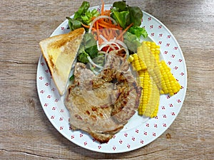 Pork chop steak with toast, steam corn and mixed salad on a plate.