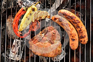 Pork chop steak and vegetable with sausage on a flaming BBQ grill.