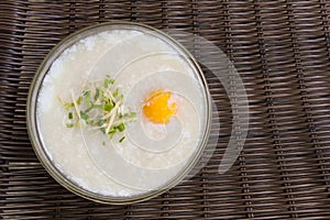 Pork chops rice porridge or congee, boiled egg and garnish with vegetable in a glass bowl.