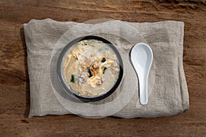 Pork congee or Chinese rice porridge with Minced pork, Egg, Enoki mushroom and Seaweed in bowl with spoon on old wooden table