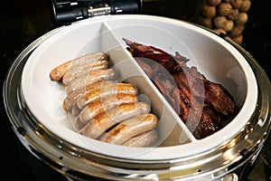 Pork crispy bacon and fried beef sausages in pan on kitchen electric stove