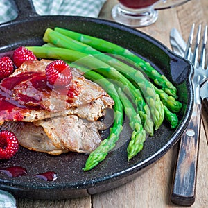 Pork cutlets with raspberry sauce and asparagus in iron cast pan, square