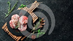 Pork cutlets wrapped in bacon served on a black plate with rosemary and thyme. On a black stone background.