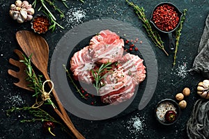 Pork cutlets wrapped in bacon served on a black plate with rosemary and thyme. On a black stone background.