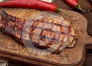 Pork fried steak on the rib lies on a vintage brown wooden board, next to fresh red chili peppers