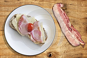 Pork Gammon Ham And Cheese Sandwich With Cherry Tomato On Porcelain Plate And Bacon Rasher Alongside Set On Old Picnic Table