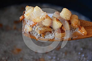 Pork greaves on a wooden ooking spoon over pot