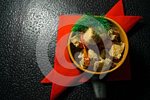 Pork in an interesting dish, baked with vegetables and decorated with dill with red napkins on a black background