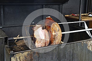 Pork leg, knuckle is fried on a spit on fire. European holiday Czech traditional dish. Grilled pork meat