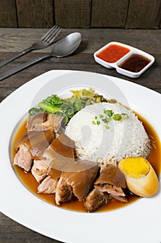 Pork leg rice with boiled egg in gravy and kale in white dish on wooden table
