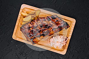 Pork loin ribs served on chopping board and potato wedges