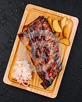 Pork loin ribs served on chopping board and potato wedges