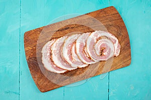 Pork meat roulade sliced on a wood chopping board, flat lay on blue table background, close up