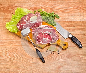 Pork neck on cutting board, meat tenderizer and kitchen knife