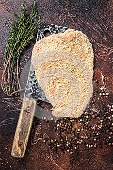 Pork Raw Escalope or schnitzel on a meat cleaver with herbs. Dark background. Top view