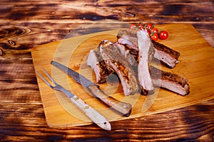 Meat pork ribs on a barbecue grill in the board on tomatoes on a wooden background flat lay