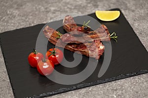 Pork ribs in barbecue sauce and honey roasted tomatoes on a black slate dish.