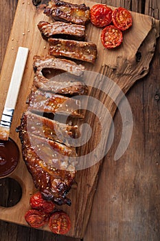 Pork ribs in barbecue sauce and honey roasted tomatoes on a wooden board. A great snack to beer on a rustic wooden table. Top view