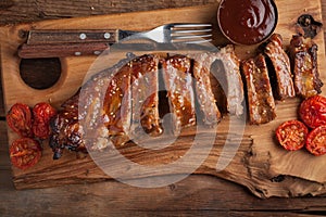 Pork ribs in barbecue sauce and honey roasted tomatoes on a wooden board. A great snack to beer on a rustic wooden table. Top view
