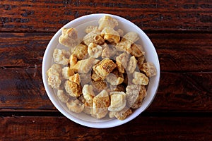 Pork rinds fried in ceramic bowl on rustic wooden table in restaurant