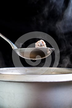 Pork rip in soup scoop with Stainless hot pot, water drop, onion and vapour on black background