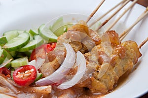 Pork satay with chili, red onion and cucumber on a white plate