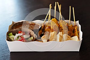 Pork Satay with peanut sauce and cucumber salad on paper food tray