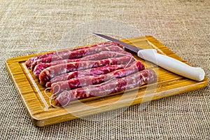 Pork sausage. thin pork sausage on wooden cutting board with knife next to it on jute fabric