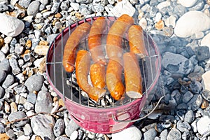 Pork sausages on portable bucket grill on stone beach