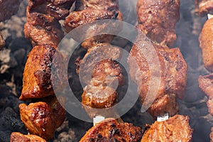 Pork shish kebab cooking on metal skewers on charcoal grill with fragrant fire smoke