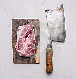 Pork steak for grilling on vintage cutting board with meat cleaver wooden rustic background top view close up