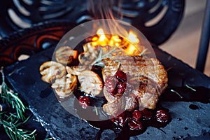 Pork steak with mushrooms and cherry sauce over vintage background on fire